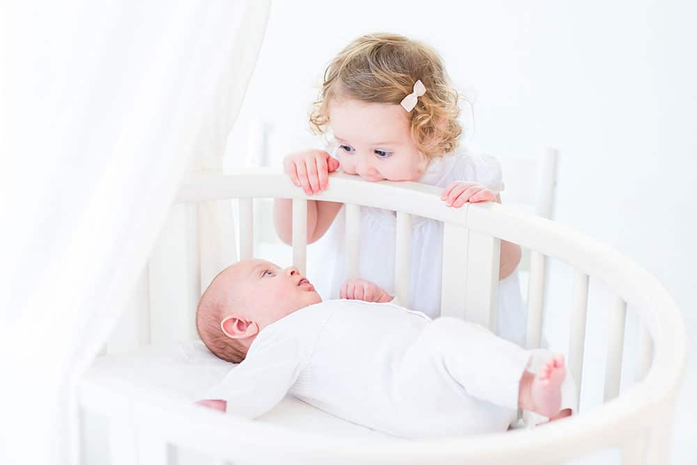 toddler looking at baby in bed