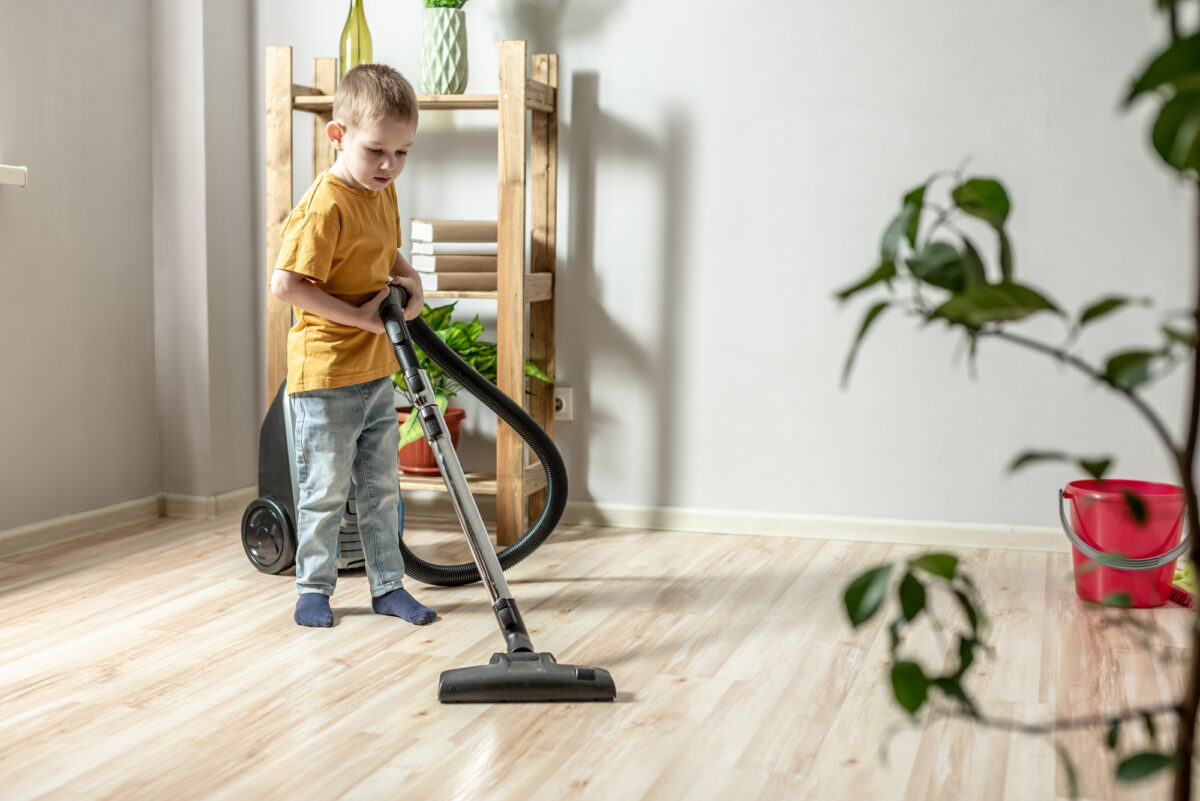 A little child helps his parents in housework, cleaning the floor using a vacuum cleaner