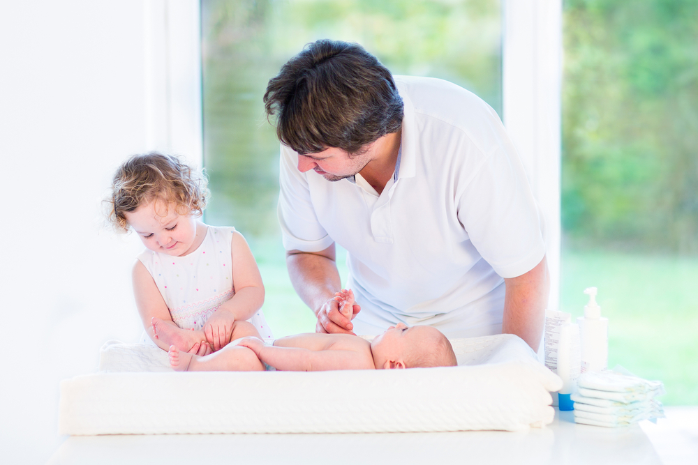 toddler helping dad change newborn sibling