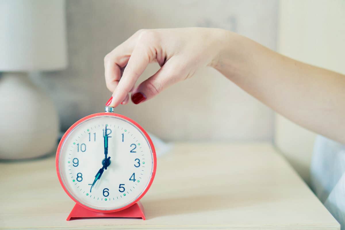 Closeup of woman hand reaching to turn off classic red alarm clock.