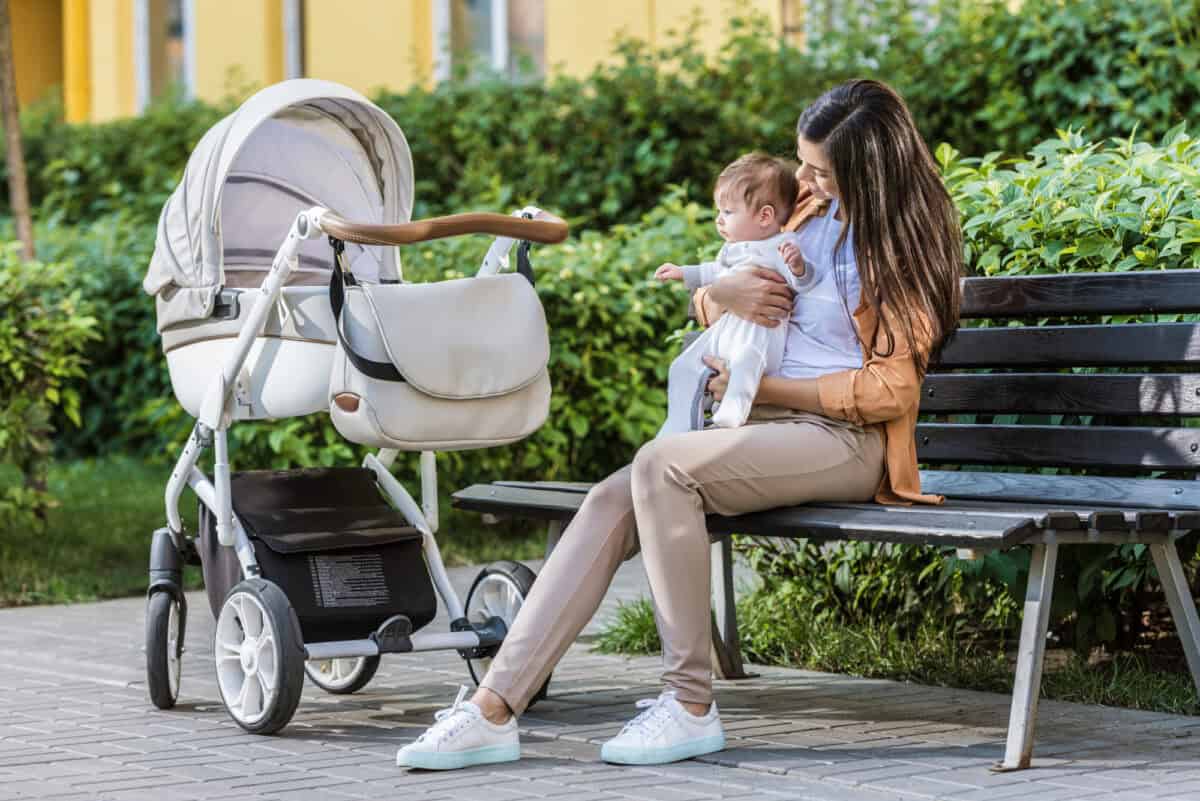 mom holding eight week old baby while using a stroller